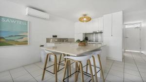 Una cocina blanca con encimera y taburetes. en Seaside On Fourth, en Sawtell 1 foto más