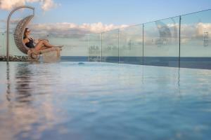 a woman sitting in a chair next to a swimming pool at Plus Fariones Suite Hotel in Puerto del Carmen