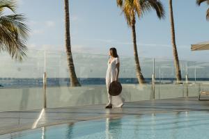 a woman in a white dress standing next to a swimming pool at Plus Fariones Suite Hotel in Puerto del Carmen