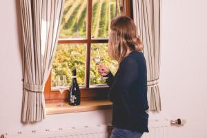 una mujer sosteniendo una copa de vino mirando por la ventana en Weingut Schwarzl, en Ratsch an der Weinstraße