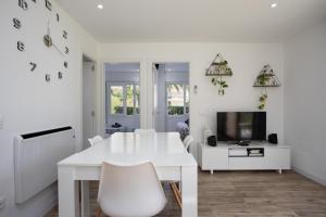 a white dining room with a white table and a tv at Apartament amb piscina i aparcament - Baixos amb jardinet in Calella de Palafrugell