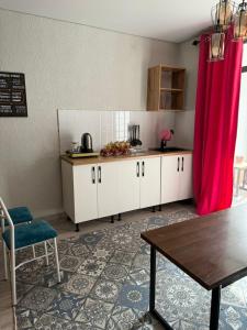 Una cocina con gabinetes blancos y una mesa y cortinas rosas. en Летняя сказка, en Cholpon-Ata