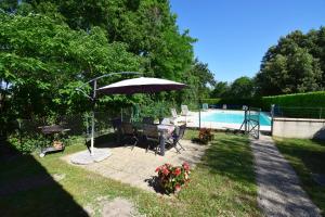 a patio with a table and an umbrella next to a pool at Ancien presbytère restauré - Gites de France 3 épis in Parranquet