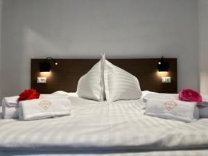 Una gran cama blanca con almohadas blancas y rosas rojas. en Hotel Angelo Boutique, en Prăjila