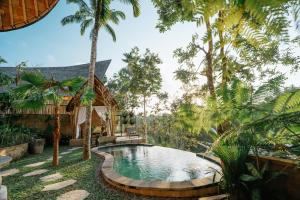 a pool in the middle of a garden with palm trees at Umah Bali Kuno Villa New in Tampaksiring