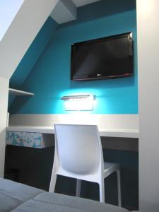 Habitación con silla y TV en la pared. en Hôtel de la Grotte, en Aix-les-Bains
