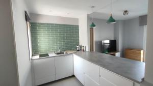 a kitchen with white cabinets and a green tile wall at Apartamento Los Corrales in Rota