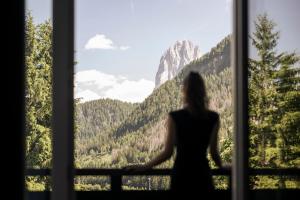 Una donna in piedi davanti a una finestra che guarda le montagne di Chalet Hotel Hartmann - Adults Only a Ortisei