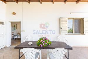 a table with white chairs and a sign on a wall at Salentoandmore - Villetta Salento in Marina San Gregorio