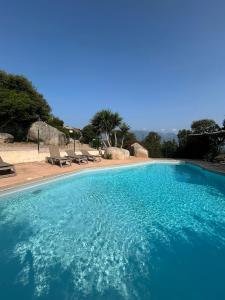 a large blue swimming pool with chairs and trees at Villa Roccapina - Porto-Vecchio in Sotta