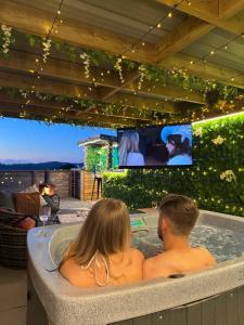 a man and woman sitting in a bathtub watching a tv at Tan Y Bryn Glamping in Conwy