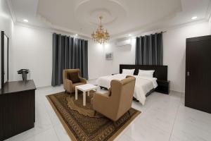 a bedroom with a bed and two chairs and a chandelier at منازل الباحة للشقق الفندقية in Al ‘Āmirah