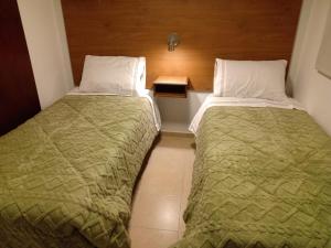 two beds in a hotel room with a green comforter at Alojamiento Guemes in San Fernando del Valle de Catamarca