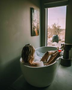 a woman laying in a bath tub in a bathroom at Heaven's Door By The Cohost Company in Pioneertown +91 photos