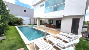 a house with a swimming pool and white chairs at Casa de praia 5 suítes Cond Pq do Jacuípe in Camaçari
