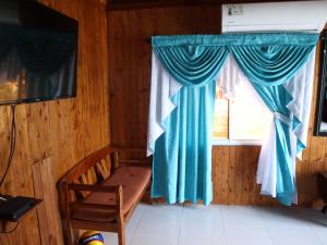 a room with a bench and a window with blue curtains at Belcys House Sapzurro in Zapzurro