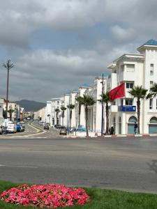a city street with buildings and pink flowers and palm trees at Résidence Al Massira Fnideq in Fnidek