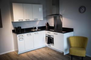 a kitchen with white cabinets and a sink and a chair at UtrechtCityApartments – Huizingalaan in Utrecht