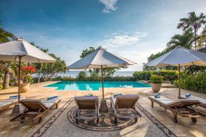 Una piscina con sillas y sombrillas al lado de una piscina. en Villa Taman Indah, en Lovina