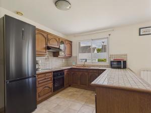 a kitchen with wooden cabinets and a stainless steel refrigerator at Maison de plain-pied pour 4 - jardin et terrasse in La Forêt-Fouesnant +12 photos