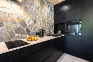 a kitchen with black cabinets and a stone wall at Apartamenty Kasztanowa Park Szczyrk in Szczyrk
