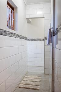 a white tiled shower with a mirror and a rug at Rock away Beach Condo. in Hartenbos