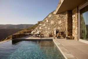 a house with a swimming pool next to a stone wall at Orias Luxury Suites Kythnos in Kithnos