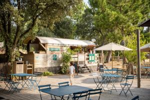 Una niña parada frente a mesas y sillas. en Huttopia Oleron Les Pins, en Saint-Trojan-les-Bains