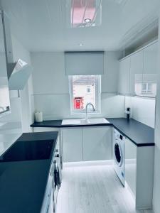 a white kitchen with a sink and a dishwasher at Modern 2 Bedroom with extra Loft Bedroom in Glasgow