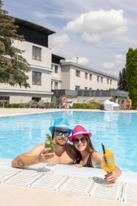a man and a woman holding drinks in a swimming pool at Hotel Atlantis in Brno