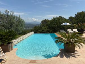 a swimming pool in a yard with chairs and an umbrella at Villa Blanc Fayence in Tourrettes
