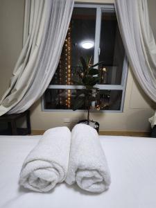 two towels sitting on a bed in front of a window at Cozy 1BR Corner with Panoramic City Skyline View in Manila