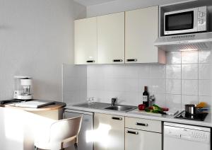 eine Küche mit weißen Schränken, einer Spüle und einer Mikrowelle in der Unterkunft At Home Appart Hotel in Toulouse