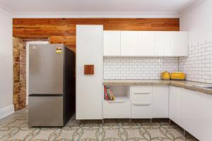 une cuisine avec des armoires blanches et un réfrigérateur en acier inoxydable dans l'établissement Stone and Timber Heritage Retreat on South Terrace, à Fremantle