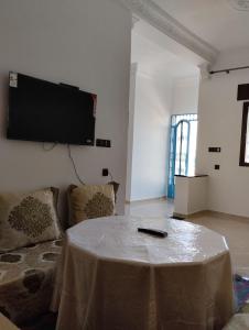 a living room with a table and a tv on the wall at Belle maison près de la plage in Chefchaouene