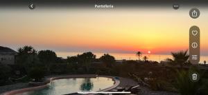 a sunset over a swimming pool with the sun setting in the background at Dammuso Kazen Jezabel in Pantelleria