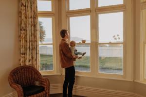 a man holding a baby standing in front of a window at Beachfront Villa, Spacious, Mountain Outlook - KK87184 in Kaikoura +17 photos