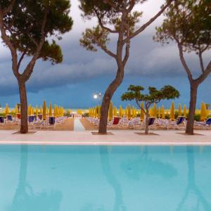 una piscina con árboles, sillas y sombrillas en Mon Repos en Lido di Jesolo