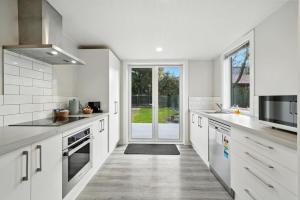 une cuisine avec des placards blancs et une grande porte dans l'établissement Albemarle Villa, à Christchurch