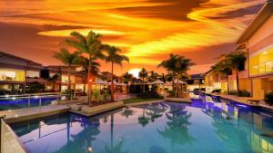 a large swimming pool with palm trees and a sunset at 1770 Lagoons Central Apartment Resort Official in Agnes Water