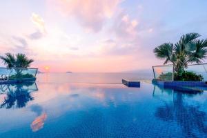 a pool with palm trees and the ocean at sunset at Boton Blue Hotel & Spa in Nha Trang