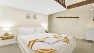 a white bedroom with a large white bed with orange and white blankets at The Loft in Culburra Beach
