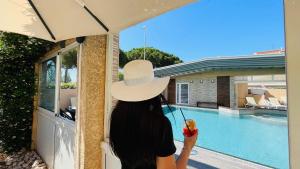 a woman wearing a hat looking out a window at a pool at Hotel & Spa Gil de France Cap d'Agde in Cap d'Agde