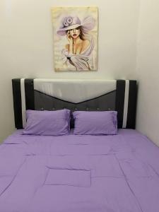 a bed with purple sheets and a painting of a woman at Himawari House Pekanbaru in Palas 2
