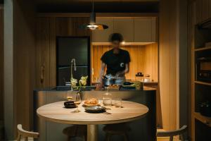 a woman is standing in a kitchen with a table at SANU 2nd Home 河口湖2nd in Fujikawaguchiko