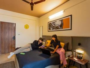 バンガロールにあるThe Hosteller Bangalore, Manyata Tech Parkのノートパソコンを持ってベッドに座っている2人の女性