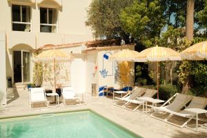 a swimming pool with lawn chairs and umbrellas at Hôtel Le Sud in Juan-les-Pins