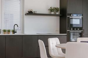 a kitchen with white chairs and a table and a microwave at Huswell - New Beach Apartment in De Haan in De Haan