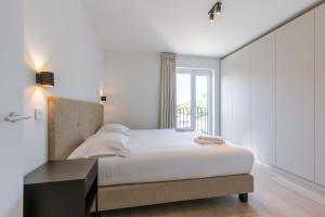 a white bedroom with a bed and a window at Huswell - New Beach Apartment in De Haan in De Haan