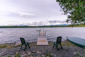 two chairs and a dock on a lake with a boat at Moose Point Cabin in Greenville